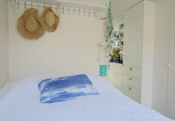 Camera da letto con cappelli di paglia, cuscino blu e arredo bianco al Beach house 'Dishoek 60', Zeeland, Paesi Bassi.