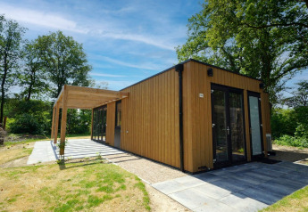 Moderne houten lodge Cube bij EuroParcs Ruinen, Nederland, omringd door bomen en blauwe lucht.