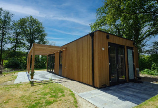 Moderno lodge in legno chiamato Cube a EuroParcs Ruinen, Paesi Bassi, circondato da alberi verdi.