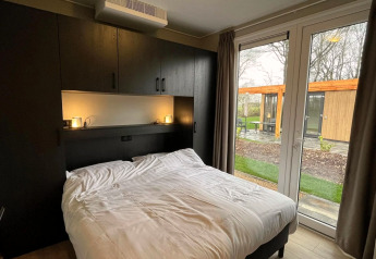 Slaapkamer met tweepersoonsbed, kasten en tuinzicht in Cube-lodge bij EuroParcs Ruinen, Nederland.