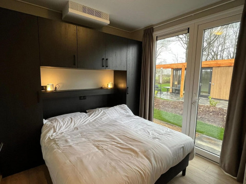 Slaapkamer met tweepersoonsbed, kasten en tuinzicht in Cube-lodge bij EuroParcs Ruinen, Nederland.