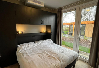 Bedroom with double bed, cabinets, and garden view at Cube lodge in EuroParcs Ruinen, Netherlands.