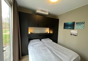 Modern lodge bedroom at Cube in EuroParcs Ruinen, Netherlands, featuring a double bed and large window.