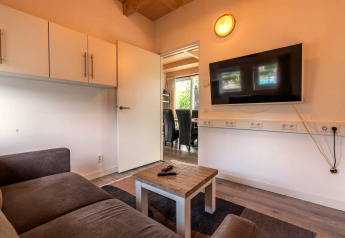 Woonkamer in Cube-lodge bij EuroParcs Ruinen, Nederland, met bank, tv, salontafel en open deur.