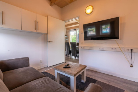 Woonkamer in Cube-lodge bij EuroParcs Ruinen, Nederland, met bank, tv, salontafel en open deur.