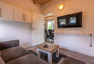 Soggiorno in una Cube lodge a EuroParcs Ruinen, Paesi Bassi, con divano, TV, tavolino e porta aperta.