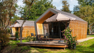 Due tiny house Solo Retreat con terrazze in legno, sedie, tavolini e ombrelloni immerse nel verde.