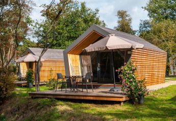 Twee Solo Retreat tiny houses met houten terrassen, tuinmeubilair en parasols in een groene omgeving.