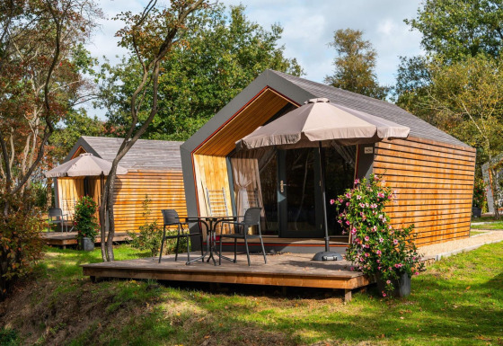 Due tiny house Solo Retreat con terrazze in legno, sedie, tavolini e ombrelloni immerse nel verde.