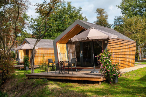 Twee Solo Retreat tiny houses met houten terrassen, tuinmeubilair en parasols in een groene omgeving.