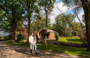 Un couple marche devant une tiny house à EuroParcs Ruinen aux Pays-Bas, entouré de verdure et d'arbres.