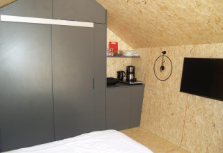 Interno di una tiny house al Solo Retreat, EuroParcs Ruinen, con letto, armadio, macchina da caffè e TV.