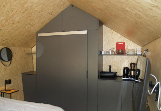 Interno di una tiny house moderna con armadi grigi, macchina da caffè e stoviglie a EuroParcs Ruinen, Paesi Bassi.