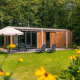 Udendørs udsigt til Cube Hot tub lodge med træfacade, terrassemøbler, parasol og grøn have i forgrunden.