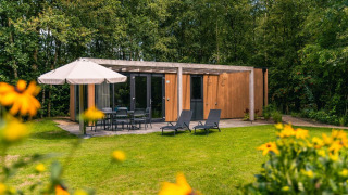 Außenansicht der Cube Hot tub Lodge mit moderner Holzfassade, Gartenmöbeln und Sonnenschirm im Grünen.