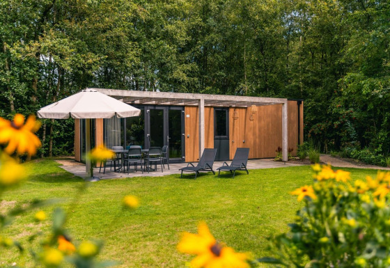 Udendørs udsigt til Cube Hot tub lodge med træfacade, terrassemøbler, parasol og grøn have i forgrunden.