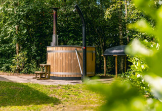 Buiten hottub van hout met schoorsteen bij Cube Hot tub lodge op EuroParcs Ruinen, Nederland, omgeven door groen.
