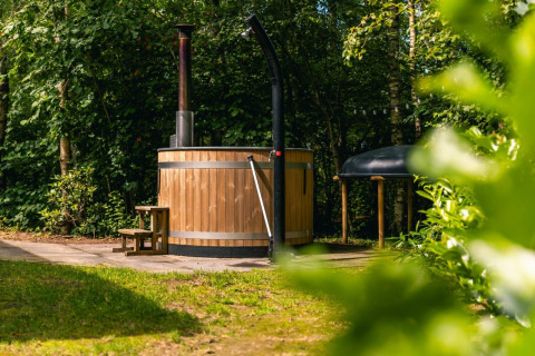 Buiten hottub van hout met schoorsteen bij Cube Hot tub lodge op EuroParcs Ruinen, Nederland, omgeven door groen.
