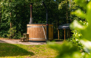 Bañera de hidromasaje de madera al aire libre en Cube Hot tub lodge en EuroParcs Ruinen, Países Bajos, rodeada de árboles.