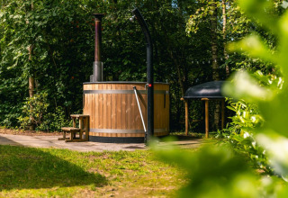 Bañera de hidromasaje de madera al aire libre en Cube Hot tub lodge en EuroParcs Ruinen, Países Bajos, rodeada de árboles.
