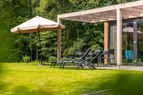 Buitenterras bij Cube Hot tub lodge in EuroParcs Ruinen, Nederland, met ligstoelen en grote parasol.