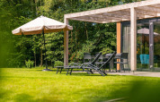 Terraza ajardinada soleada en Cube Hot tub lodge de EuroParcs Ruinen, Países Bajos, con tumbonas y sombrilla.