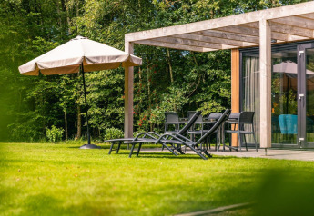 Terraza ajardinada soleada en Cube Hot tub lodge de EuroParcs Ruinen, Países Bajos, con tumbonas y sombrilla.