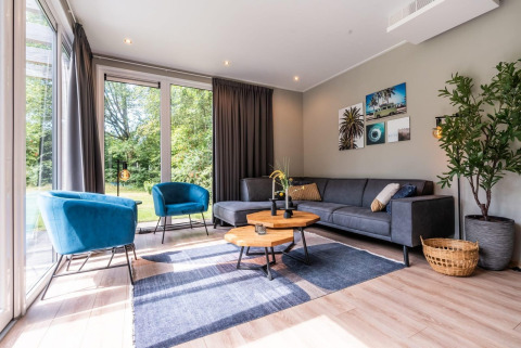 Moderne woonkamer met blauwe stoelen en grijze bank in Cube Hot tub lodge bij EuroParcs Ruinen.