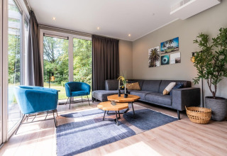 Soggiorno moderno con poltrone blu e divano grigio nel Cube Hot tub lodge a EuroParcs Ruinen, Paesi Bassi.