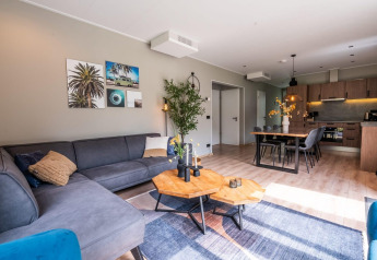 Modernes Wohnzimmer mit grauem Sofa, Holztisch und offener Küche in Cube Hot tub Lodge bei EuroParcs Ruinen.