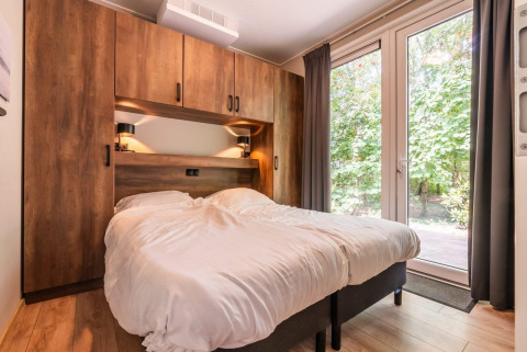 Acogedor dormitorio en la cabaña Cube Hot tub de EuroParcs Ruinen con cama doble y vista al bosque.