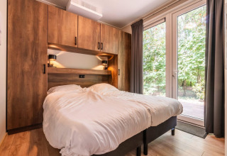 Gezellige slaapkamer in de Cube Hot tub-lodge bij EuroParcs Ruinen met dubbel bed en zicht op bos.