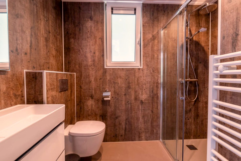 Modern badkamer met houtlook muren, glazen douche en raam bij Cube Hot tub, EuroParcs Ruinen, Nederland.