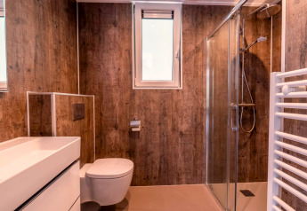 Modern badkamer met houtlook muren, glazen douche en raam bij Cube Hot tub, EuroParcs Ruinen, Nederland.