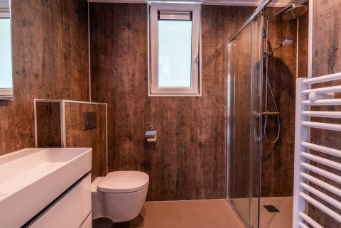Bagno moderno con pareti effetto legno, doccia in vetro e finestra al Cube Hot tub, EuroParcs Ruinen, Paesi Bassi.