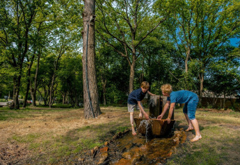 Deux enfants jouent près d’une source d’eau extérieure entourée d’arbres dans un hébergement glamping.