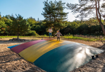 Kinderen spelen op een grote kleurrijke springkussen in het zand op een glampinglocatie tussen de bomen.