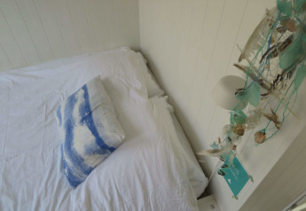Camera luminosa con lenzuola bianche, cuscino blu marino e decorazioni costiere al Beach house Dishoek 60.