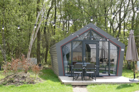 Tiny house chiamata Solo Retreat nel bosco, con luci appese e arredo da esterno su terrazza.
