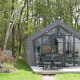 Et lille hus kaldet Solo Retreat i en skov, med terrasse, havemøbler og lyskæder i det grønne.