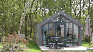 Pequeña casa llamada Solo Retreat en el bosque, con luces y muebles de exterior en una terraza.