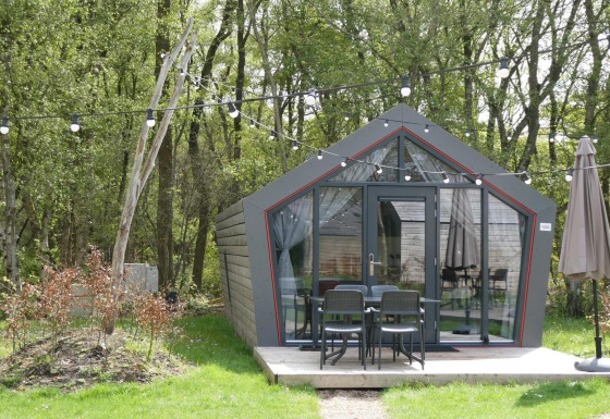 Et lille hus kaldet Solo Retreat i en skov, med terrasse, havemøbler og lyskæder i det grønne.
