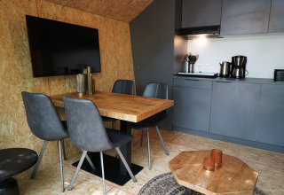 Zona pranzo e cucina moderna in tiny house con sedie grigie, tavolo in legno e TV a EuroParcs Ruinen.