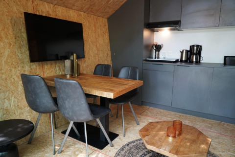 Coin repas et cuisine moderne en tiny house avec chaises grises, table en bois et TV à EuroParcs Ruinen.