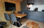 Moderne Tiny House Küche und Essbereich mit grauen Stühlen, Holztisch und TV im EuroParcs Ruinen.