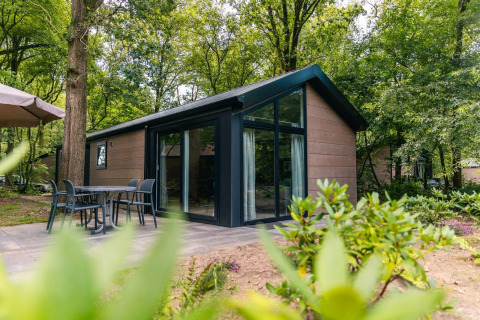 Moderne Velthorst-lodge met glazen gevel, terras met stoelen, midden in een groene bosrijke omgeving.