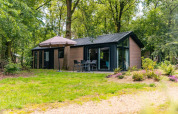 Moderne Lodge Velthorst bei EuroParcs Ruinen, Niederlande, im Grünen mit Gartenmöbeln und Sonnenschirm.