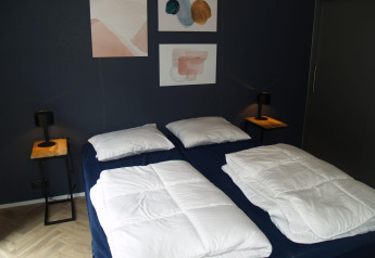 Slaapkamer met twee enkele bedden, blauwe muren, abstracte kunst en houten tafels bij Velthorst, EuroParcs Ruinen.