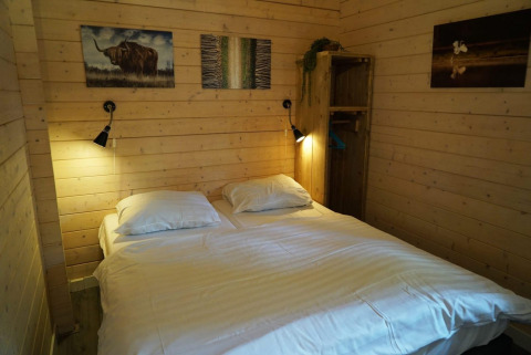 Camera da letto con letto matrimoniale, pareti in legno, lampade e arte al Drentse kap, EuroParcs Ruinen, Paesi Bassi.