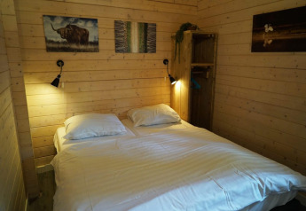 Dormitorio con cama doble, paredes de madera, lámparas de pared y arte en Drentse kap, EuroParcs Ruinen, Países Bajos.